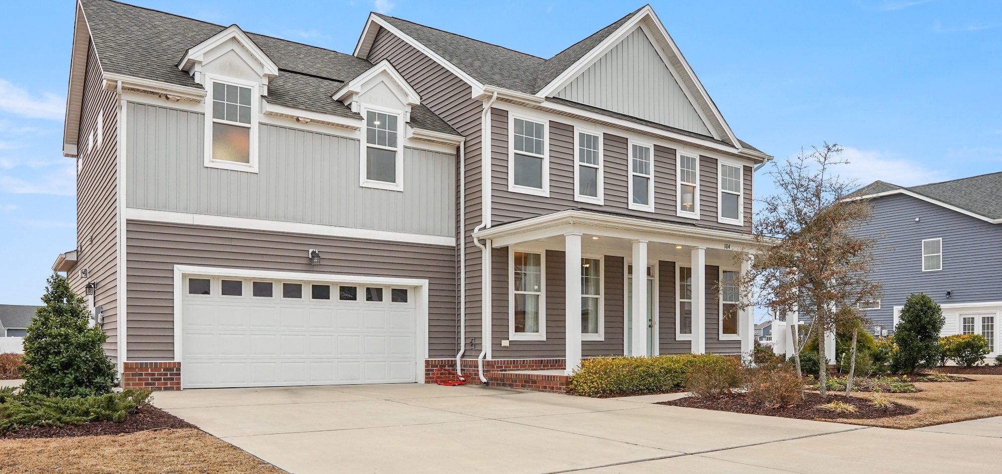 Two-story gray house with white trim, front porch, and landscaped yard.