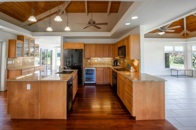 Spacious kitchen with wooden cabinetry, dark appliances, and an island, featuring a ceiling fan.