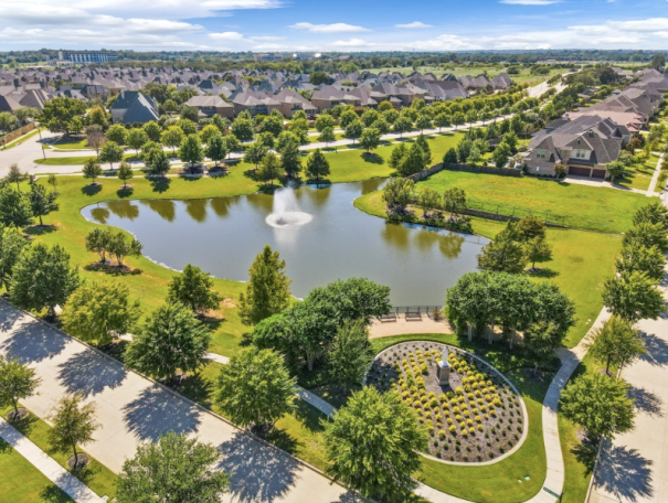 Aerial view of a neighborhood with a pond, fountain, and landscaped gardens.