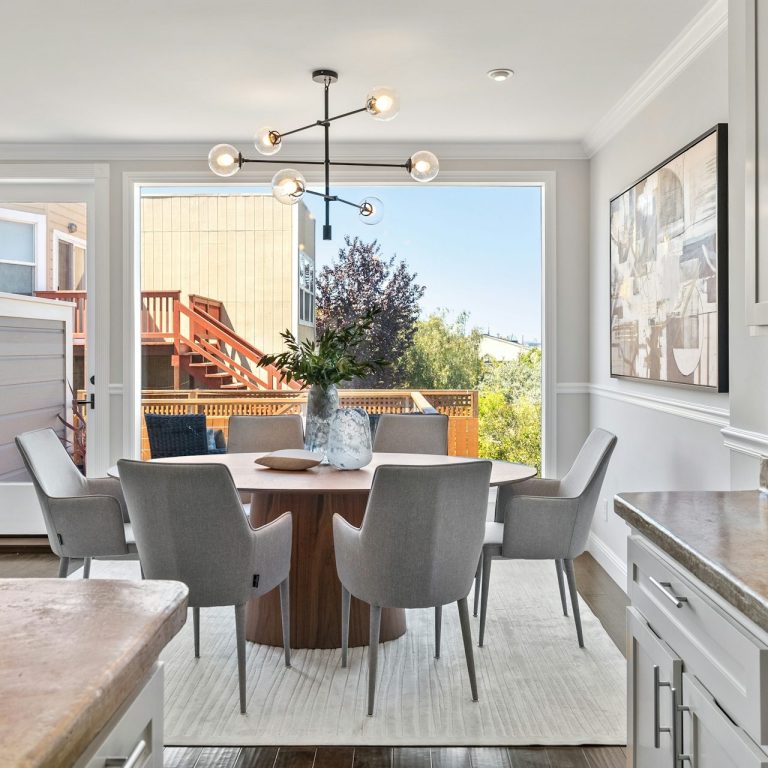 Modern dining area with a round table, gray chairs, and large windows overlooking a patio.
