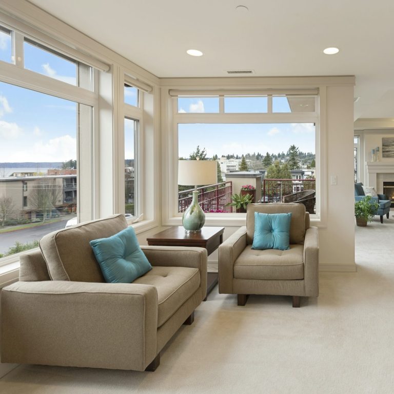 Bright living room with large windows, two armchairs, and a table. Scenic view outside.