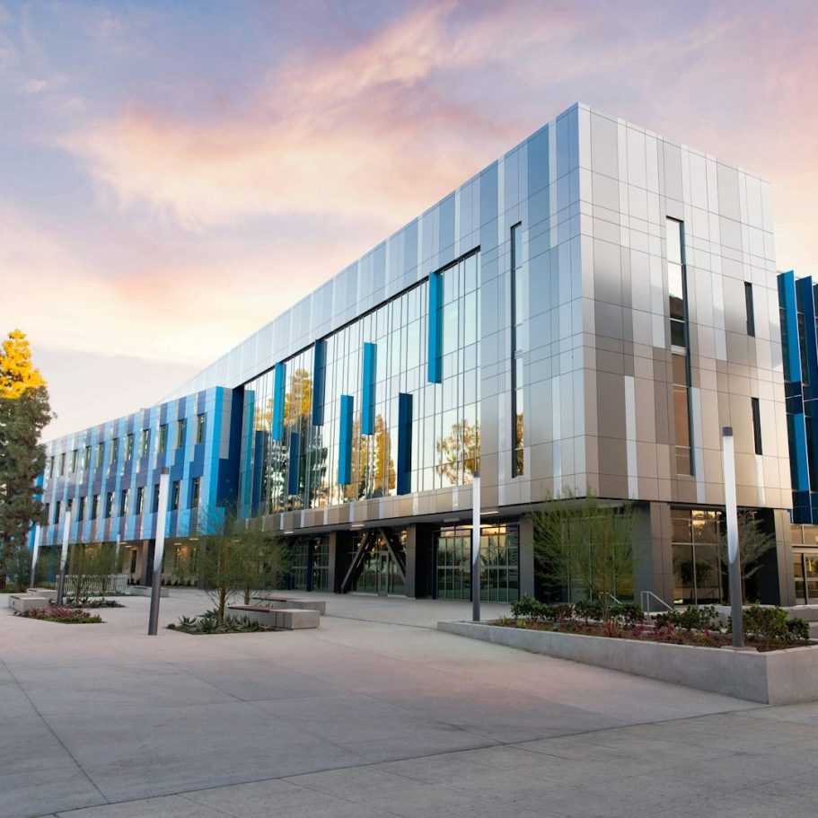 Modern building with a sleek metallic facade and large blue accents, surrounded by landscaping.