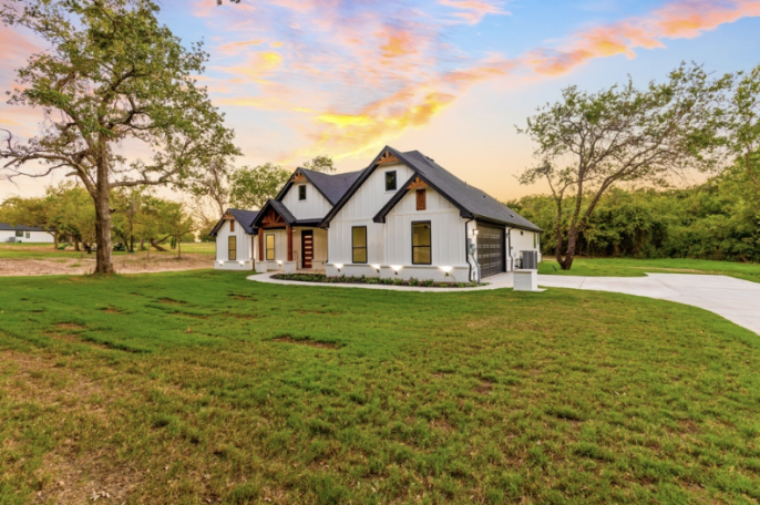 Modern white farmhouse surrounded by greenery at sunset.
