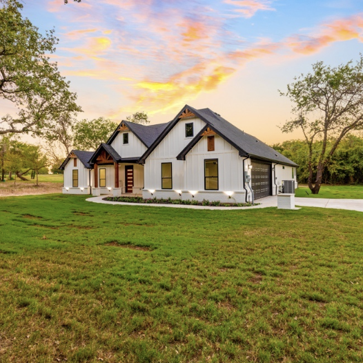 Modern house with a dark roof and white walls, surrounded by a green lawn and sunset sky.
