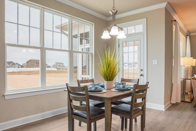 Bright dining area with a table, chairs, and a plant, featuring large windows.