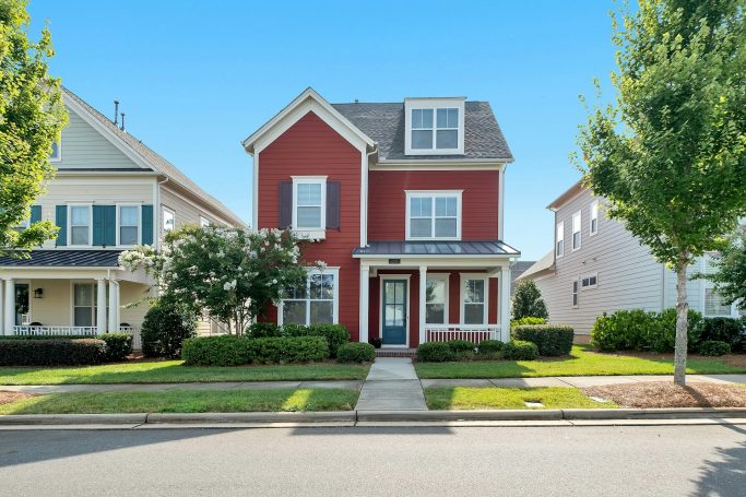 Red two-story house with white trim, surrounded by green lawns and trees.
