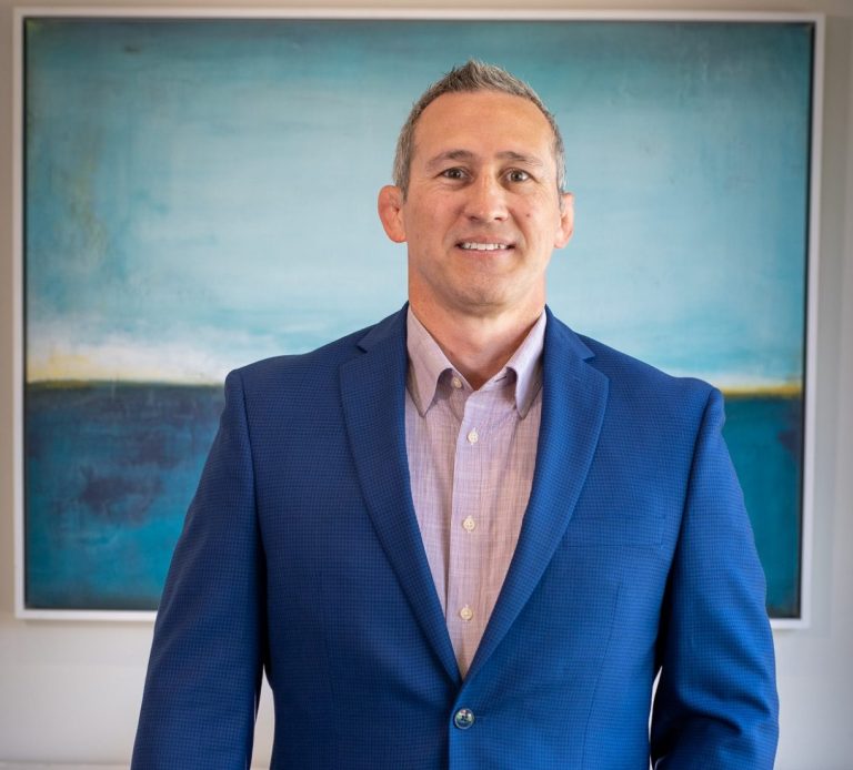 Man in a blue suit standing in front of a large abstract painting. Chad McPhatter